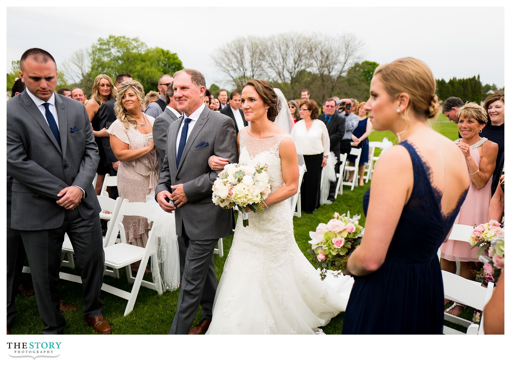 bride walks with father down the aisle at outdoor wedding ceremony at Hiland Park