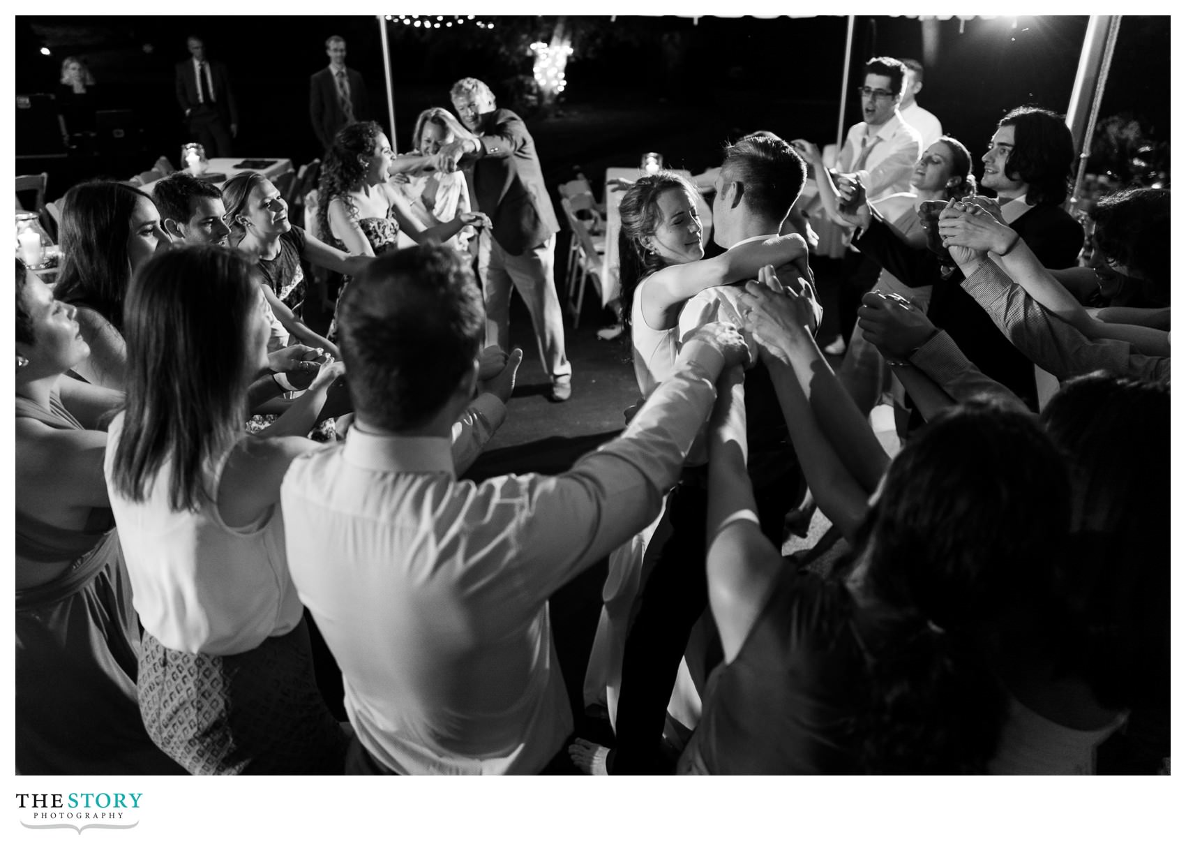 wedding guests dance with bride and groom at tent wedding reception on Skaneateles Lake