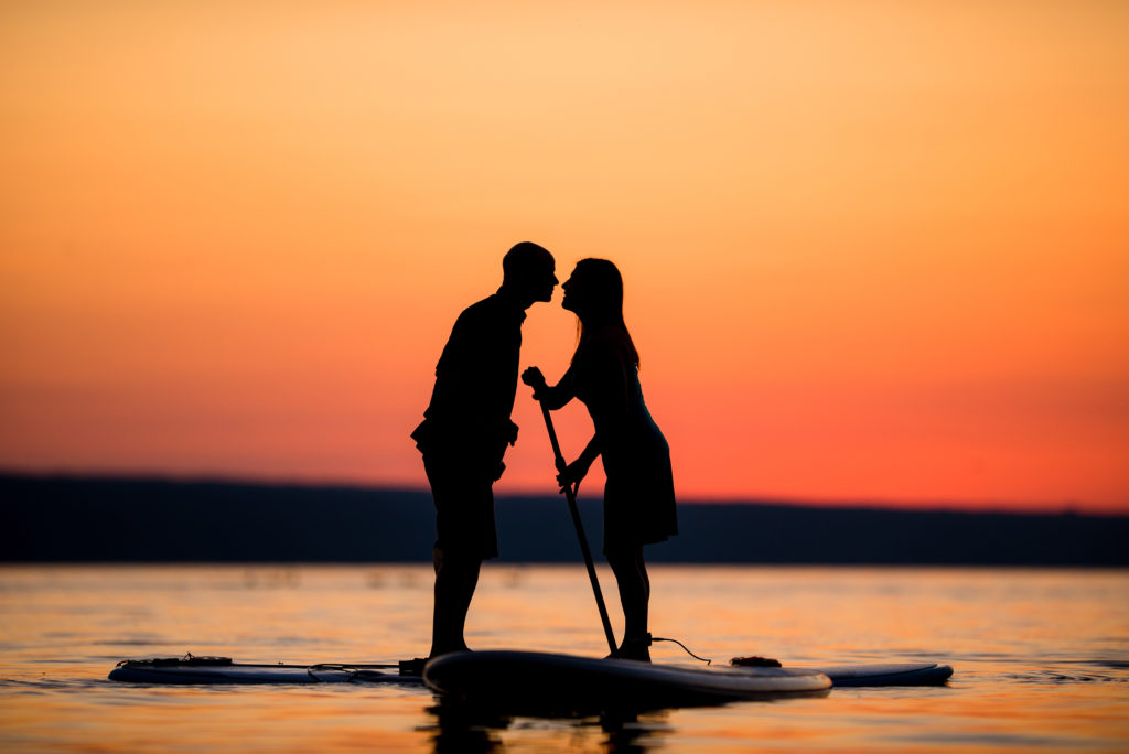 engagement photo of couple paddle boarding on Cayuga Lake at sunset 