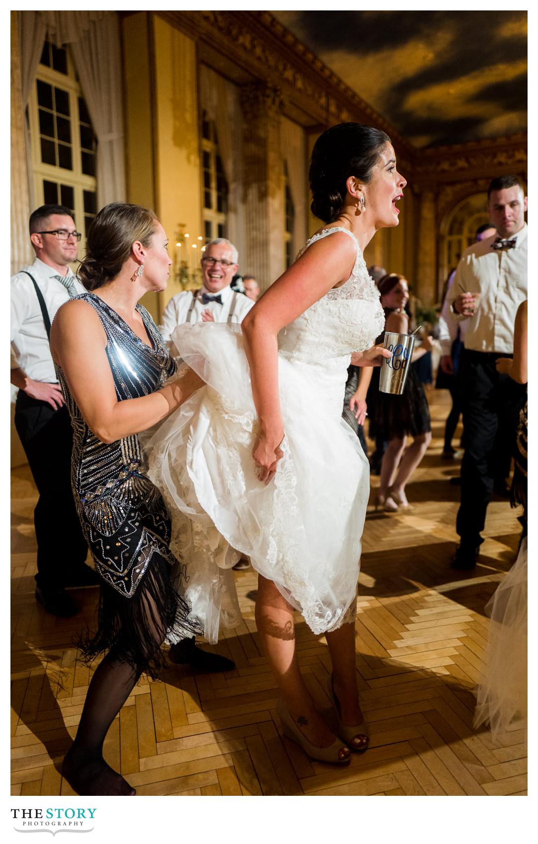 friend of bride holds up her dress at wedding reception in downtown Syracuse